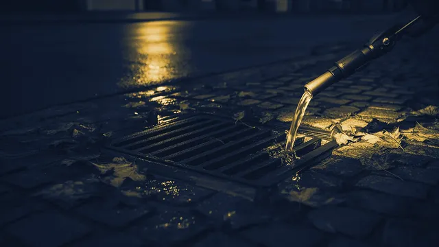Straatkolk met bladeren waar regenwater in wegloopt, avondlicht